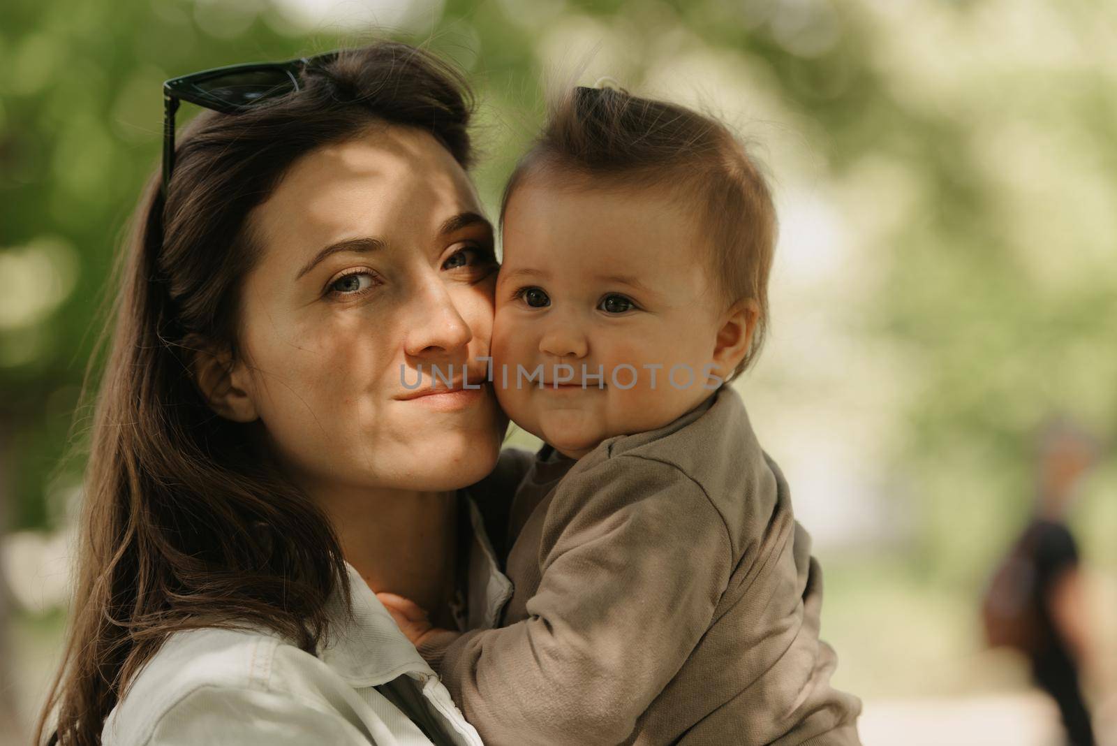 A young mother is holding in her arms her 7-month daughter in the park. A mom is enjoying her infant daughter in the woodland.