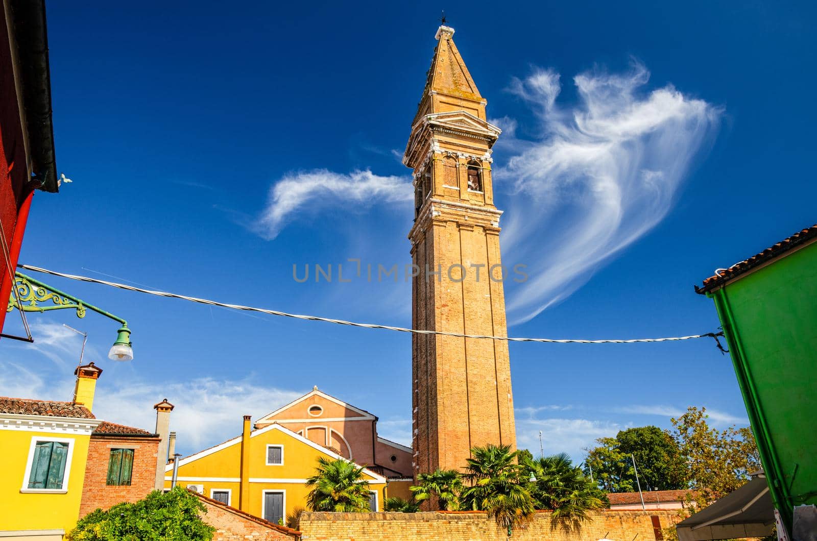 San Martino Roman Catholic church in Burano island with brick bell tower campanile, blue sky background in sunny summer day, Venice Province, Veneto Region, Northern Italy. Burano postcard