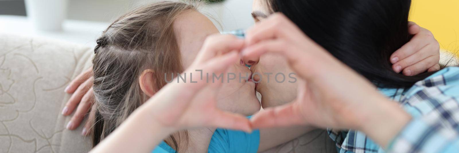 Mom kisses little daughter, together show heart gesture by kuprevich