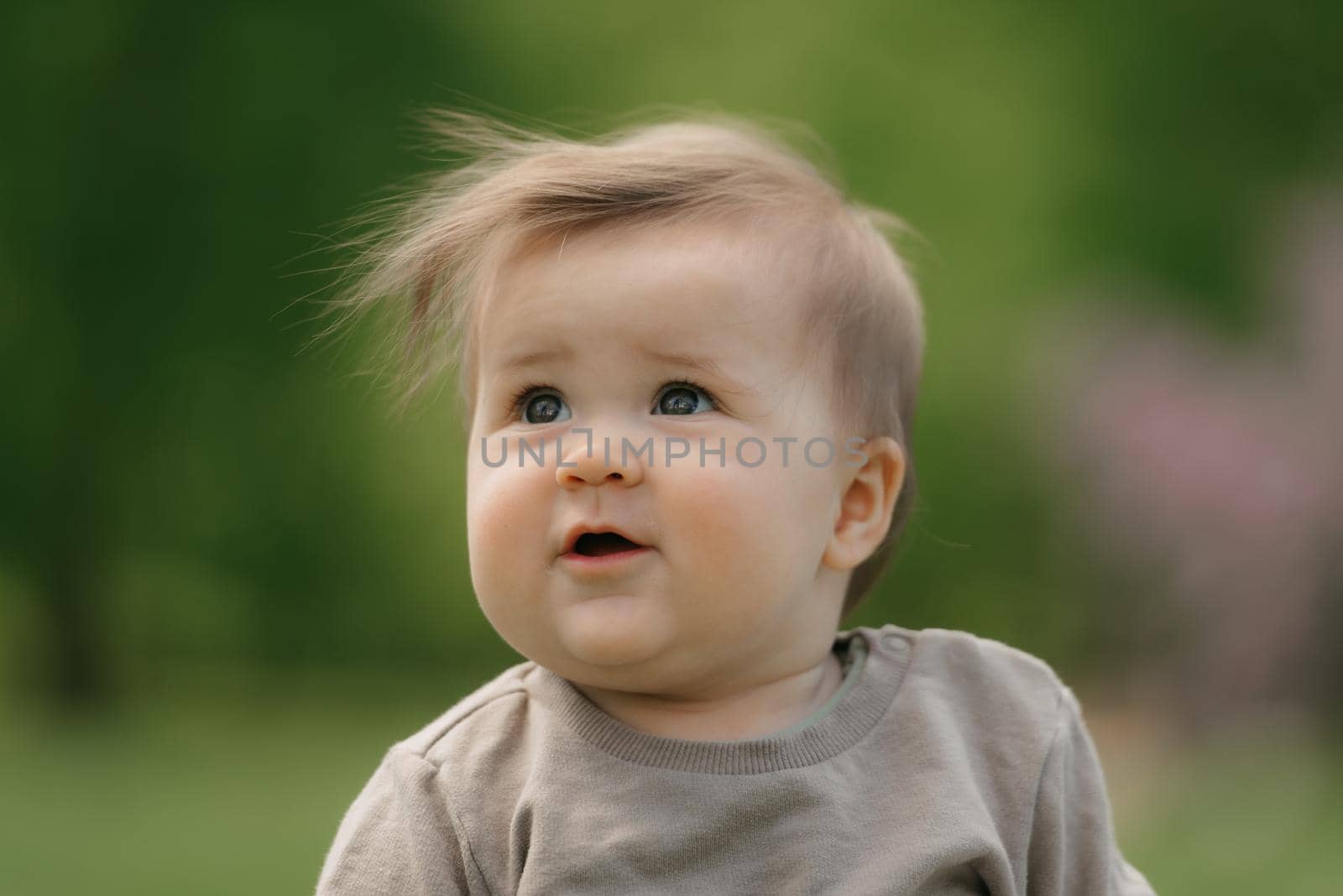 A close portrait of a cute 7-month child who is playing in the meadow. An infant girl is crawling on the grass.