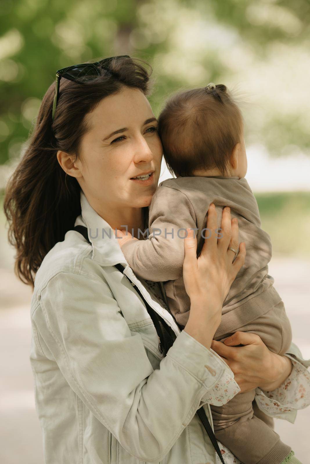 A heroic mother is holding in her arms her 7-month daughter in the park. A mom is happy with her infant daughter in the woodland.