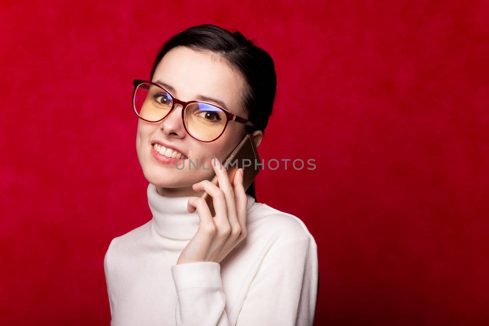 woman in a white turtleneck talking on the phone, portrait on a red background by shilovskaya