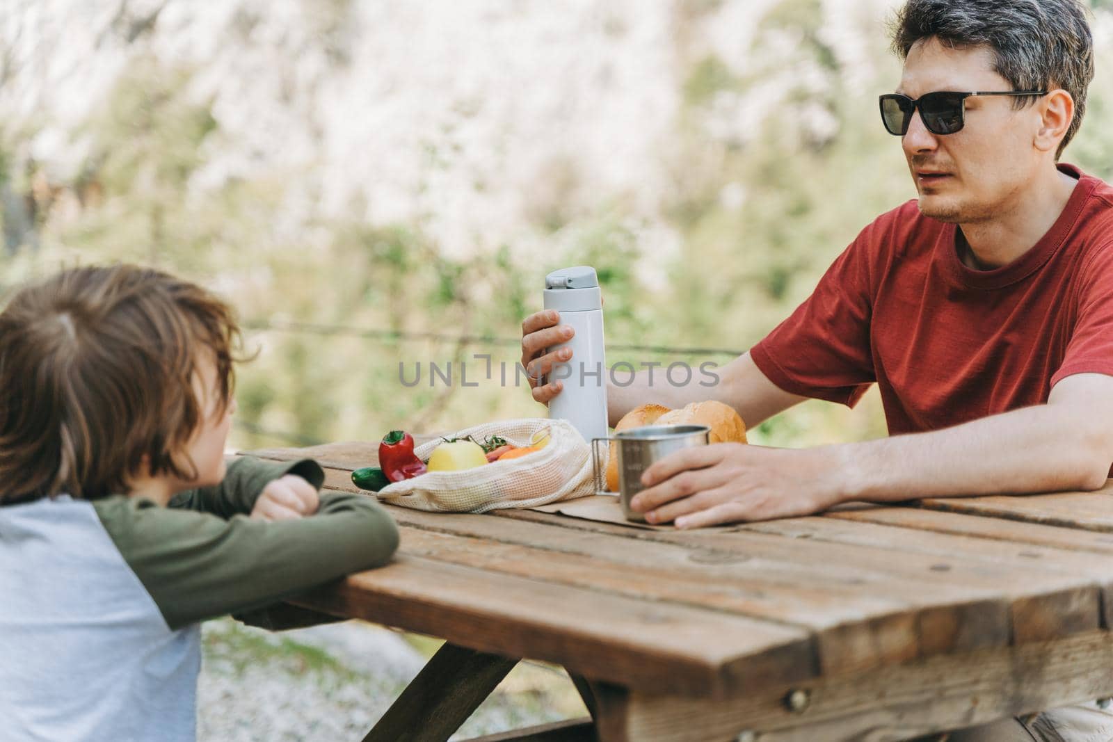 Close-up view of father and his school boy son on a family picnic in the mountains. Child kid and his dad taking a rest and enjoying a picnic while hiking in the mountains by Ostanina