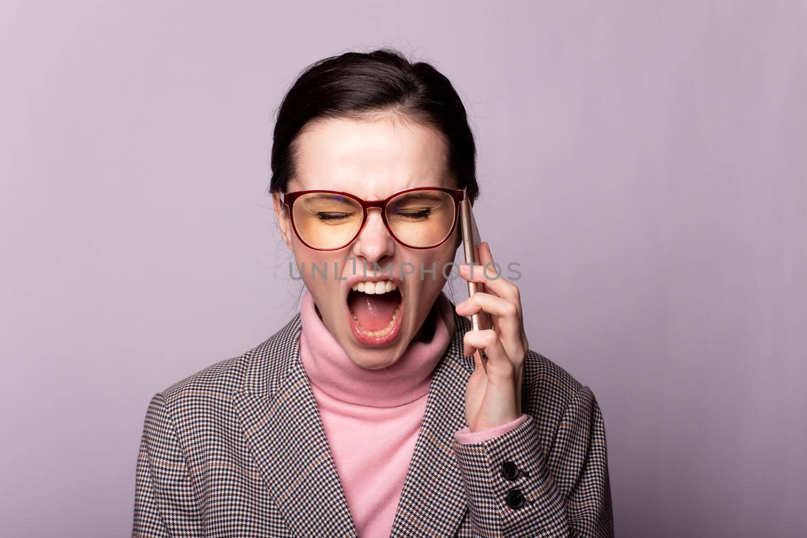 woman in a pink turtleneck, gray jacket, glasses for sight communicates on the phone on a gray background. High quality photo