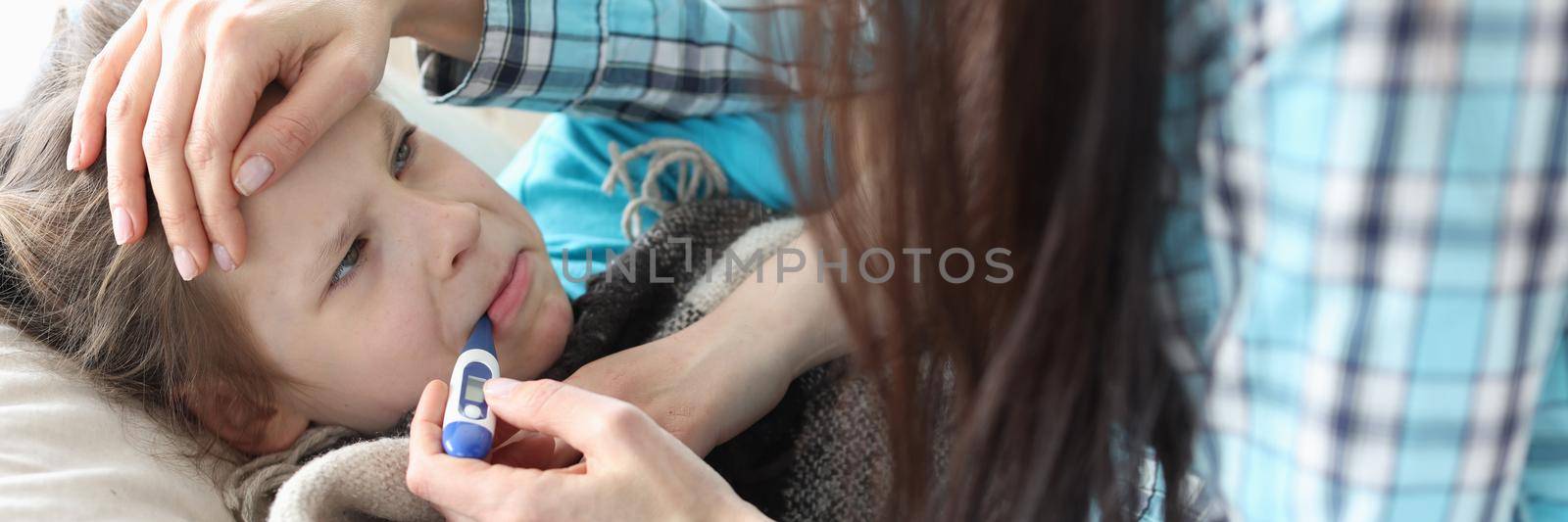 A dissatisfied girl with a thermometer in her mouth, her mother is nearby. Family health control, childhood illnesses