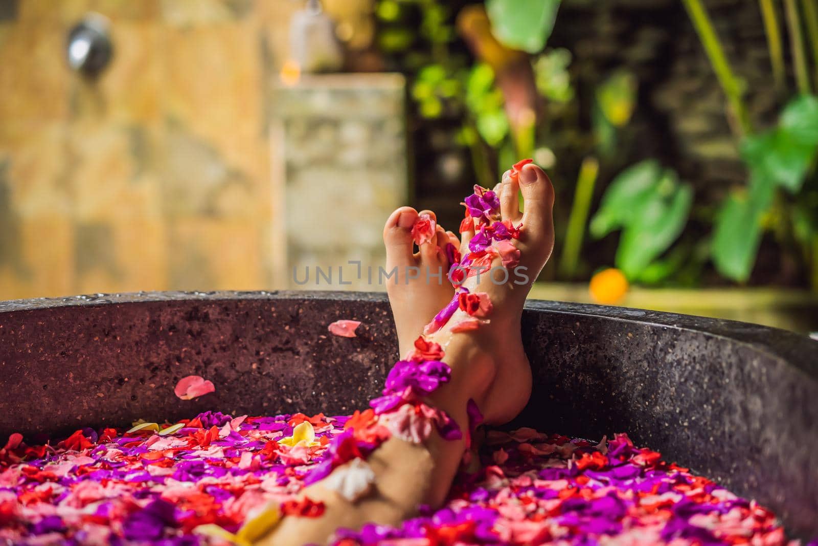 Attractive Young woman in bath with petals of tropical flowers and aroma oils. Spa treatments for skin rejuvenation. Alluring woman in Spa salon. Girl relaxing in bathtub with flower petals. Luxury.