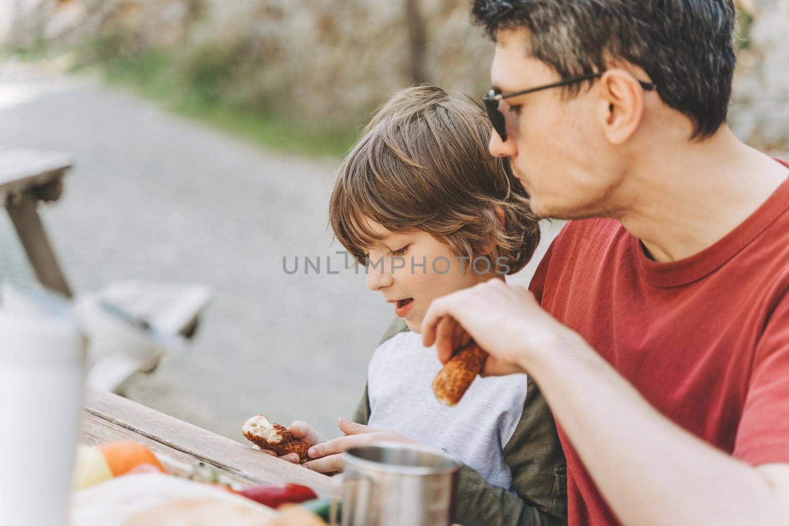 Close-up view of father hugs his school boy son on a family picnic in the mountains. Child kid and his dad taking a rest and enjoying a picnic while hiking in the mountains by Ostanina