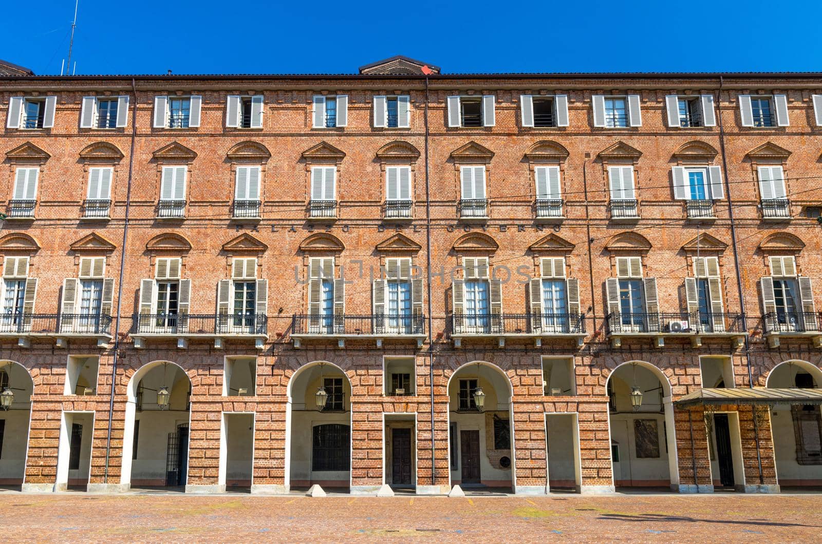 Prefecture Palazzo del Governo Palace brick building with arches, windows and shutters on Castle Square Piazza Castello in historical centre of Turin Torino city with clear blue sky, Piedmont, Italy