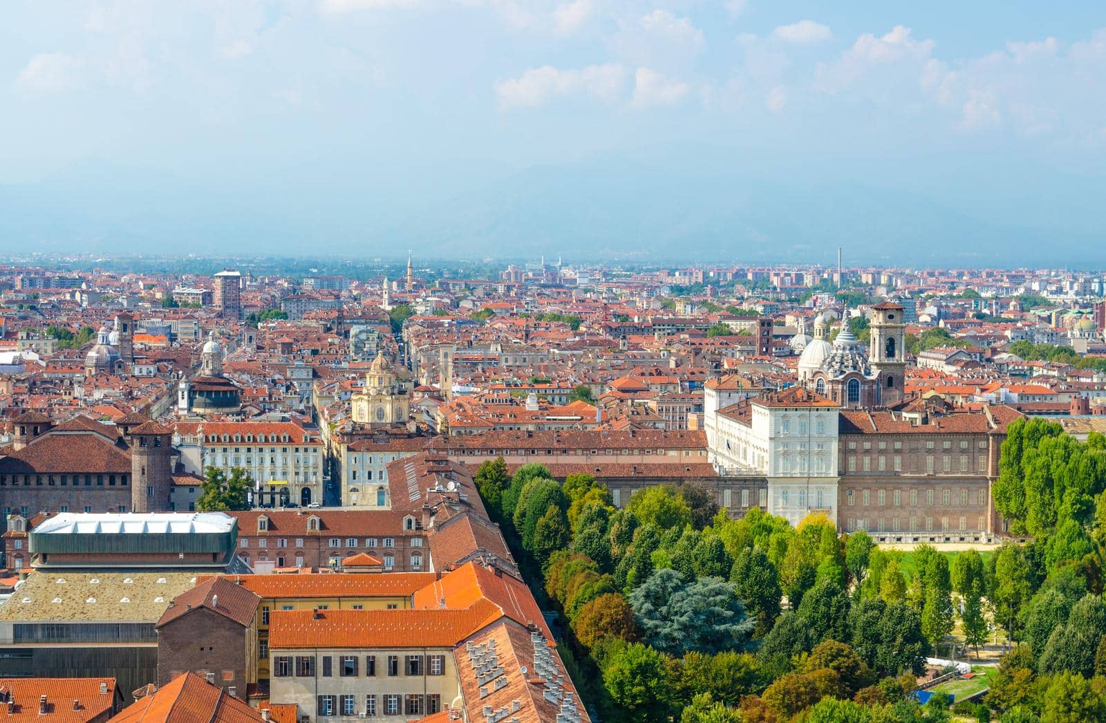 Aerial top panoramic view of Turin city historical centre with Royal Palace, San Lorenzo church, orange tiled roofs of buildings, Giardini Reali gardens park with Alps mountain range, Piedmont, Italy