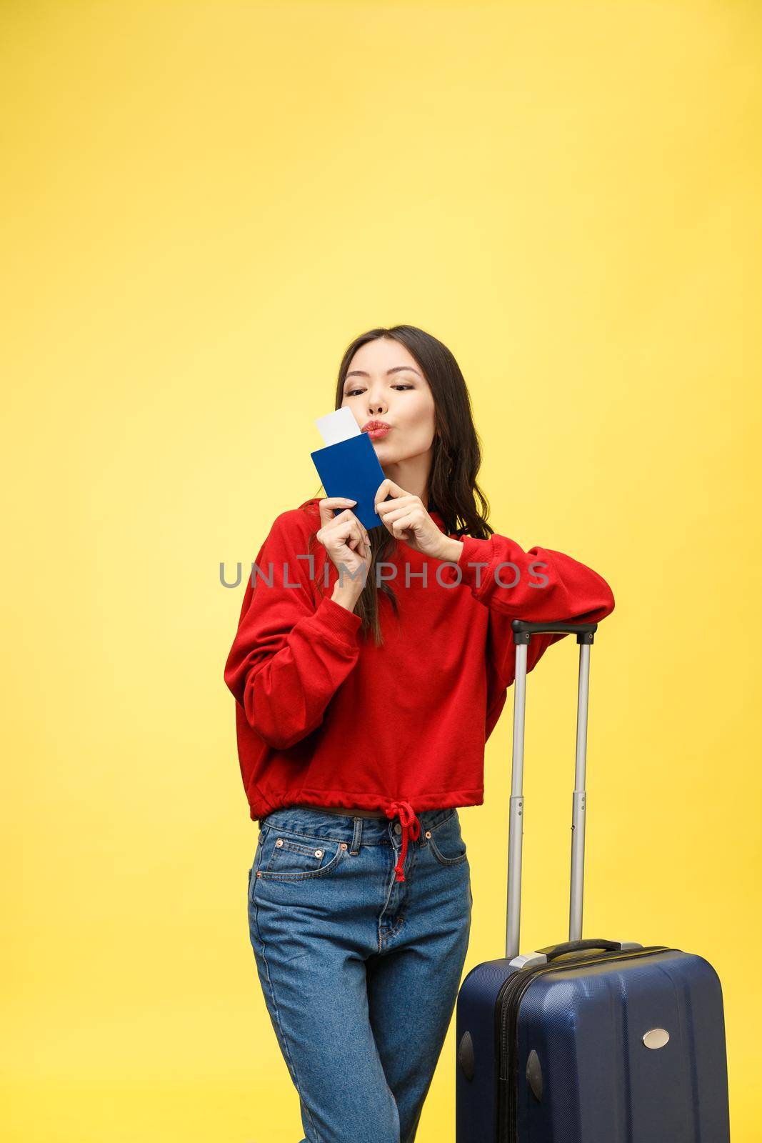 Woman travel. Young beautiful asian woman traveler with suitcase and passport on yellow background.