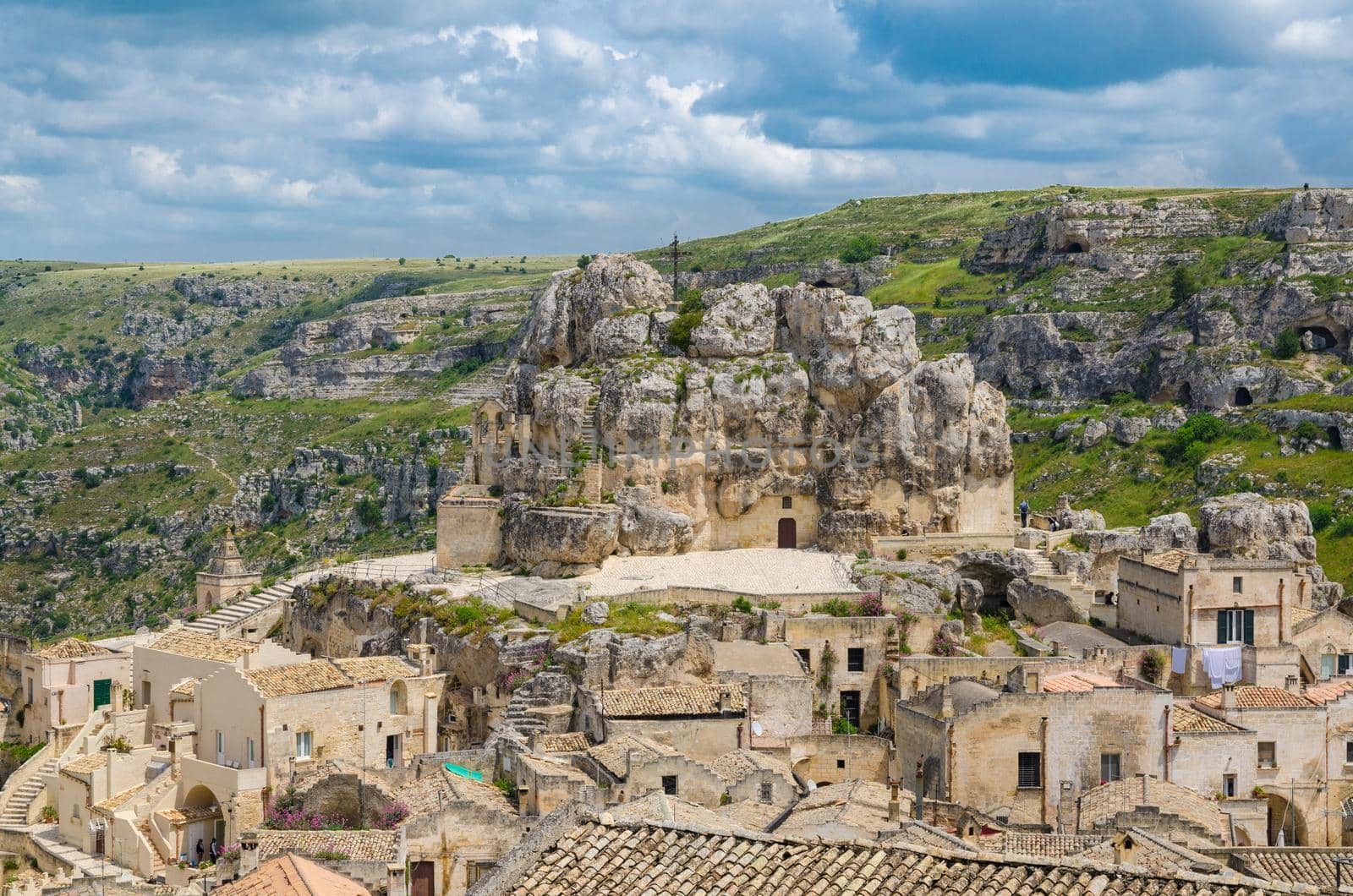 Rock church Santa Maria De Idris with big cross in historical centre of old ancient town Sassi di Matera in front of caves di Murgia Timone and dramatic sky, UNESCO, Basilicata, Southern Italy