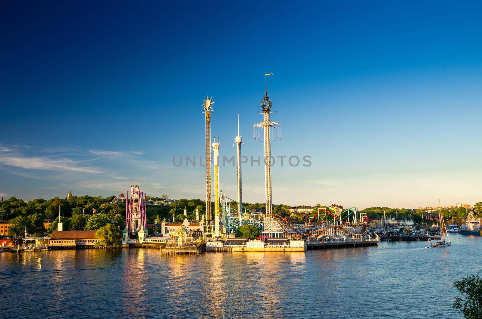 Djurgarden island and Tivoli carousel amusement attractions Grona Lund (Luna Park) with green forest and blue sky background and water of Lake Malaren view from Skeppsholmen island, Stockholm, Sweden