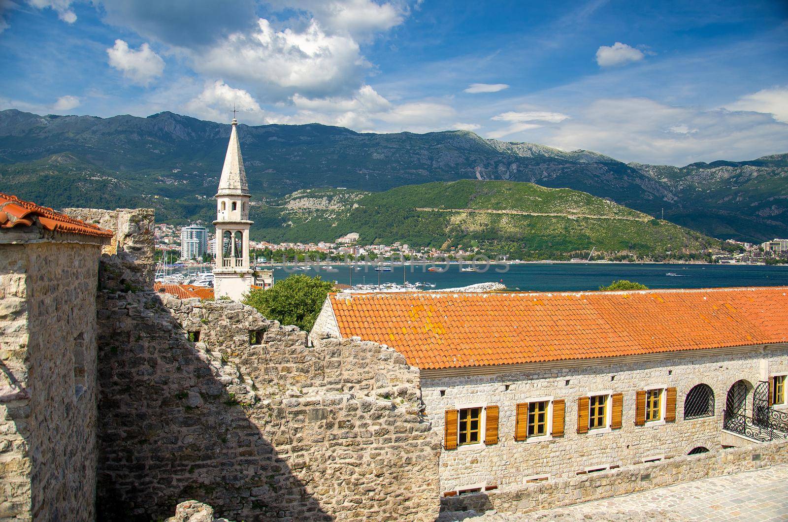 Stone citadel fortress in Old town Budva with view of medieval buildings, red tiled roofs, chapel of Saint Ivan church, marine, bay, range of mountains and Adriatic Riviera, Montenegro