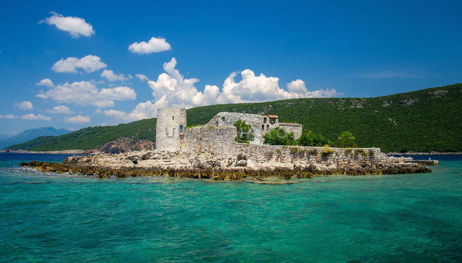 Monastery and church Vavedenja Presvete Bogorodice on island Mala Gospa near Zanjic on Lustica peninsula, Boka Kotor bay with blue turquoise paradise water, blue sky, white clouds, Montenegro