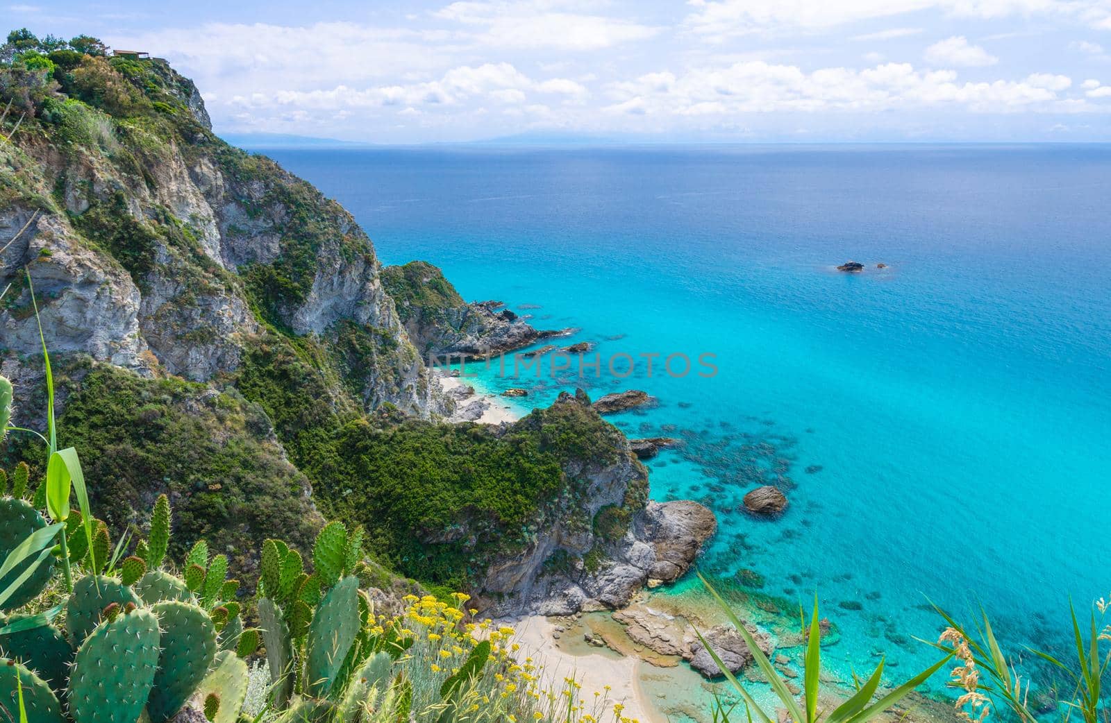 Rock cliff of cape Capo Vaticano Ricadi aerial panoramic view from Parco Belvedere platform, green grass hill with amazing blue azure turquoise water, blue sky background, Calabria, Southern Italy