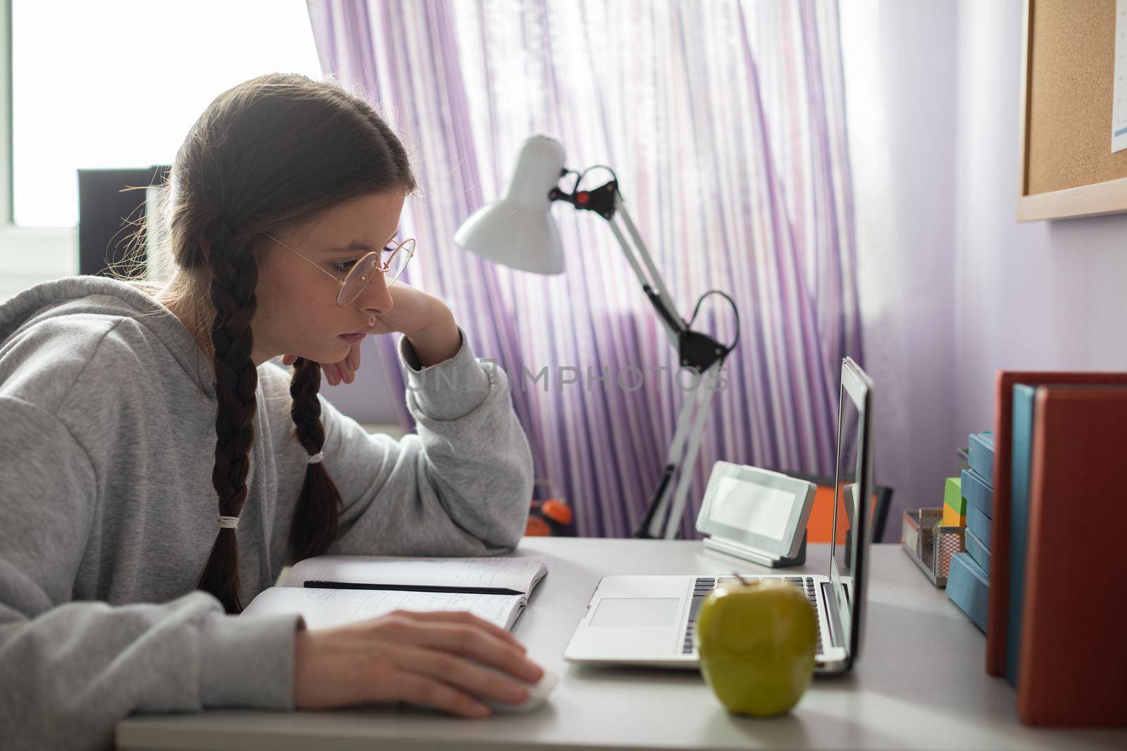 A student sits at her desk and studies using the internet and a personal computer. A diligent student. Remote learning at home.