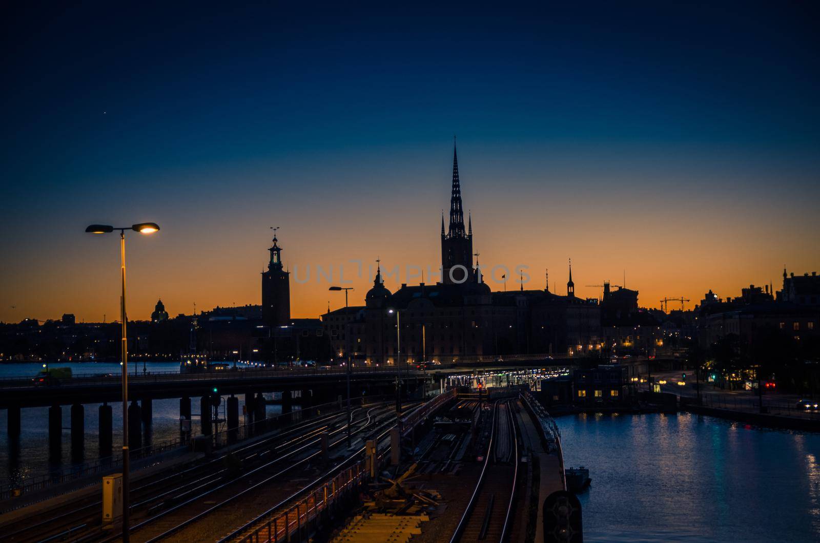 Silhouette of Stockholm cityscape skyline with Riddarholmen Church spires, City Hall Stadshuset tower, bridge over Lake Malaren in Gamla Stan at sunset, dusk, twilight and blue orange sky, Sweden