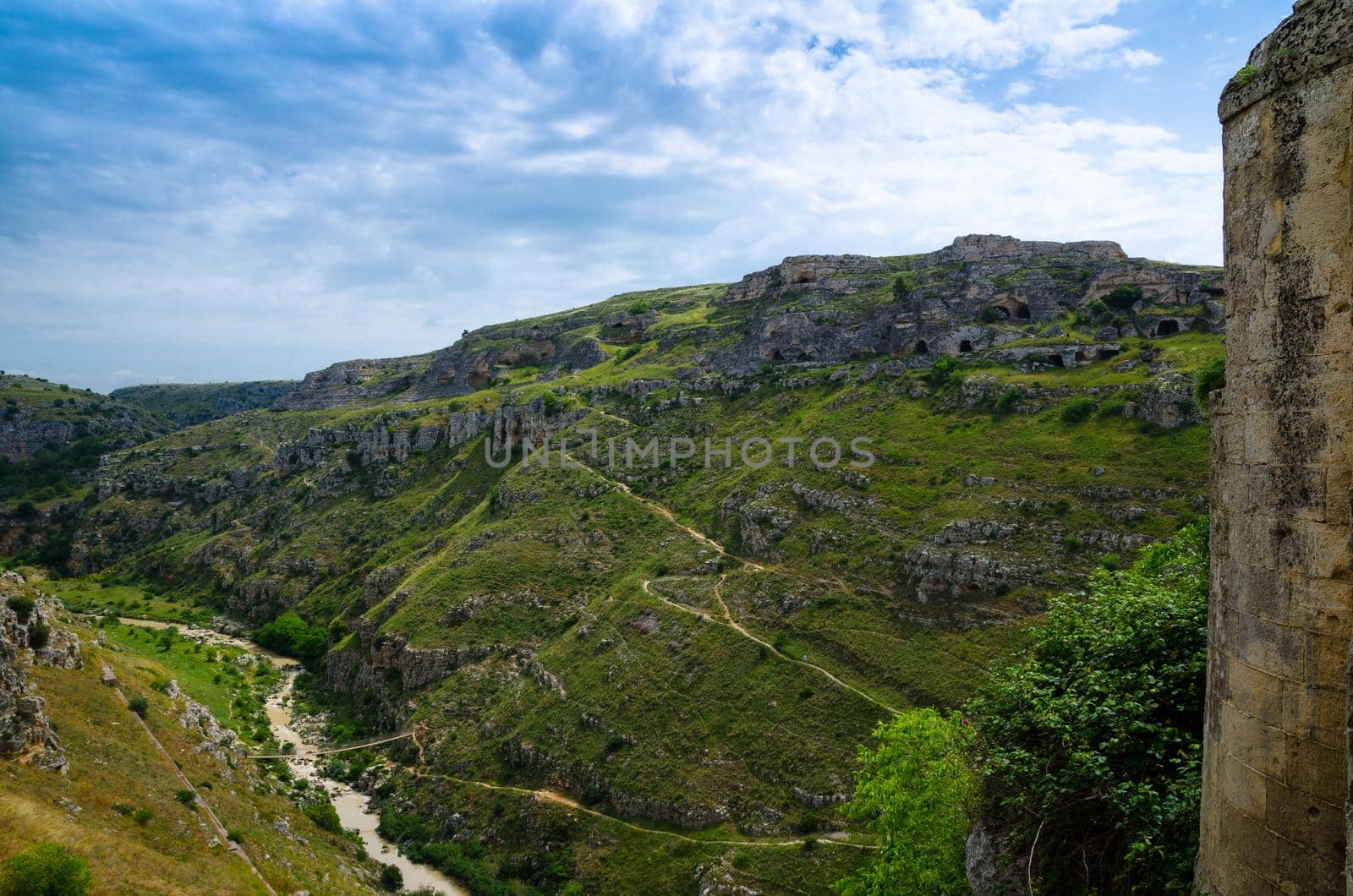 View of ravine canyon with rocks and houses in caves di Murgia Timone near old ancient town Matera (Sassi) with blue sky ant white clouds, UNESCO World Heritage, Basilicata, Southern Italy