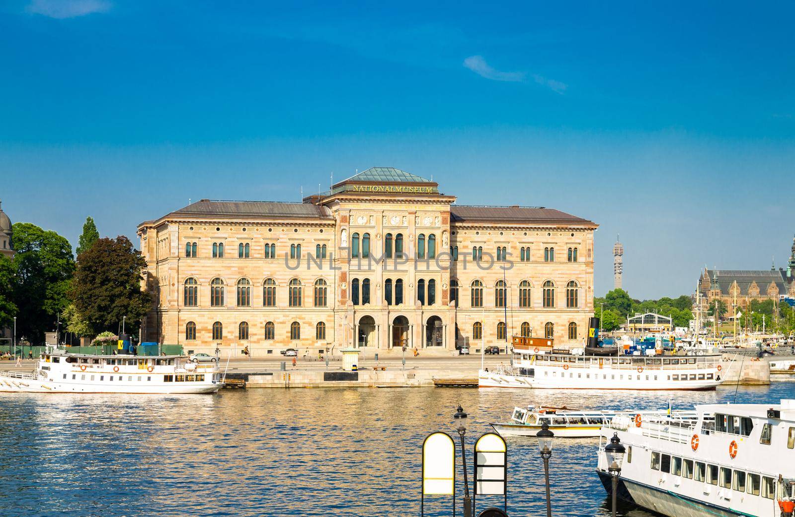 National Museum of Fine Arts (Nationalmuseum) building located on peninsula Blasieholmen in city centre with white boats, ships on Lake Malaren water, blue sky background, Stockholm, Sweden