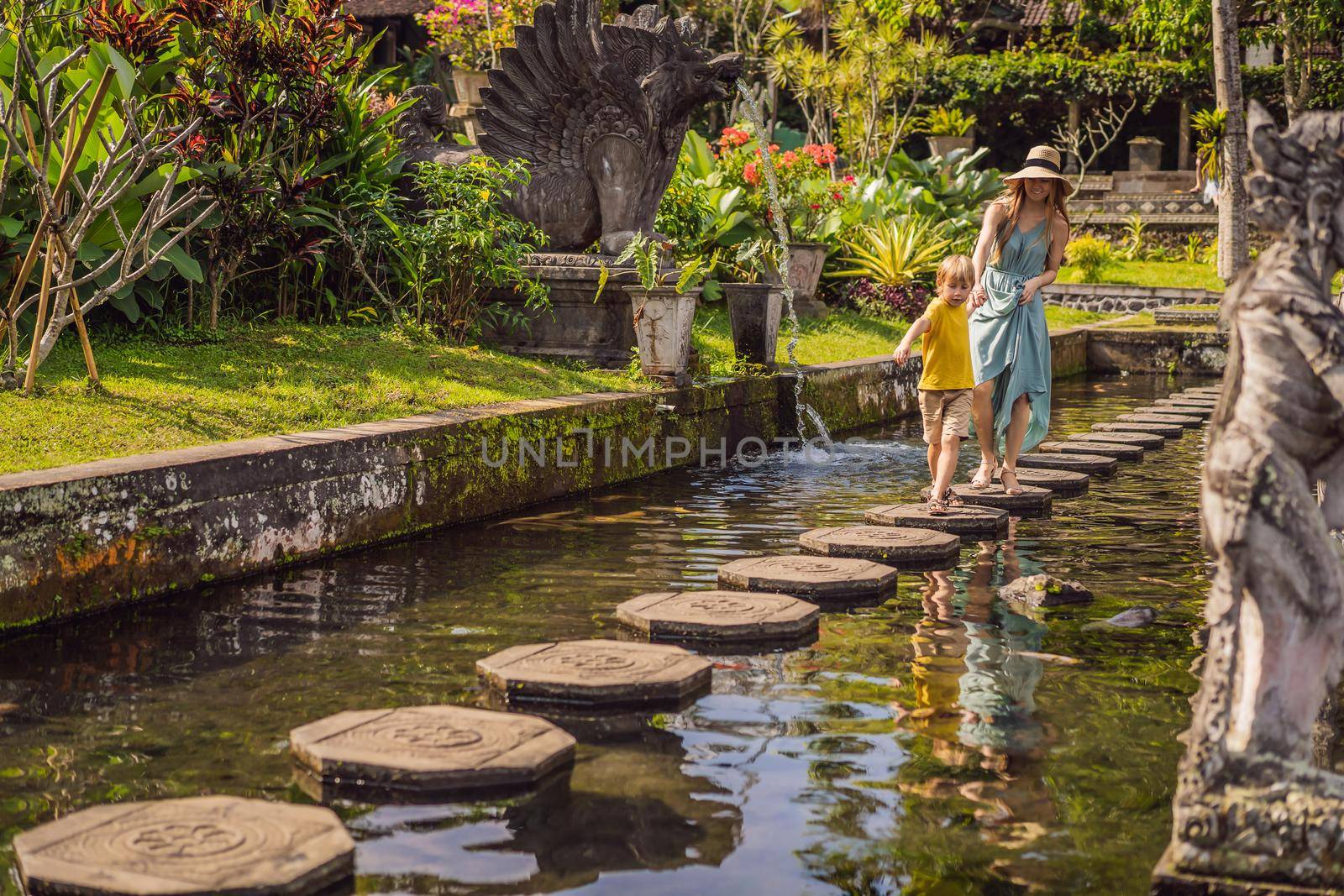 Mom and son tourists in Taman Tirtagangga, Water palace, Water park, Bali Indonesia. Honeymoon in Bali. Traveling with children concept. Kids friendly place.