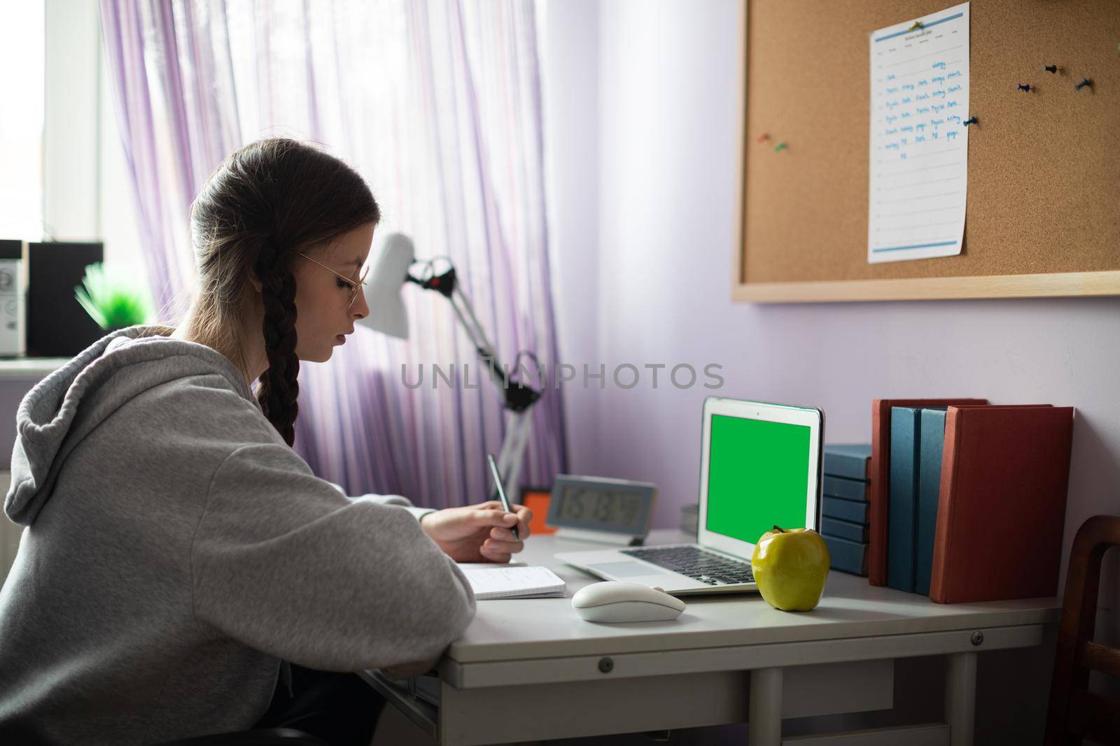 Green screen on laptop. At home in her room, a teenager sits at her desk solving assignments from school. A diligent student. Remote learning at home.