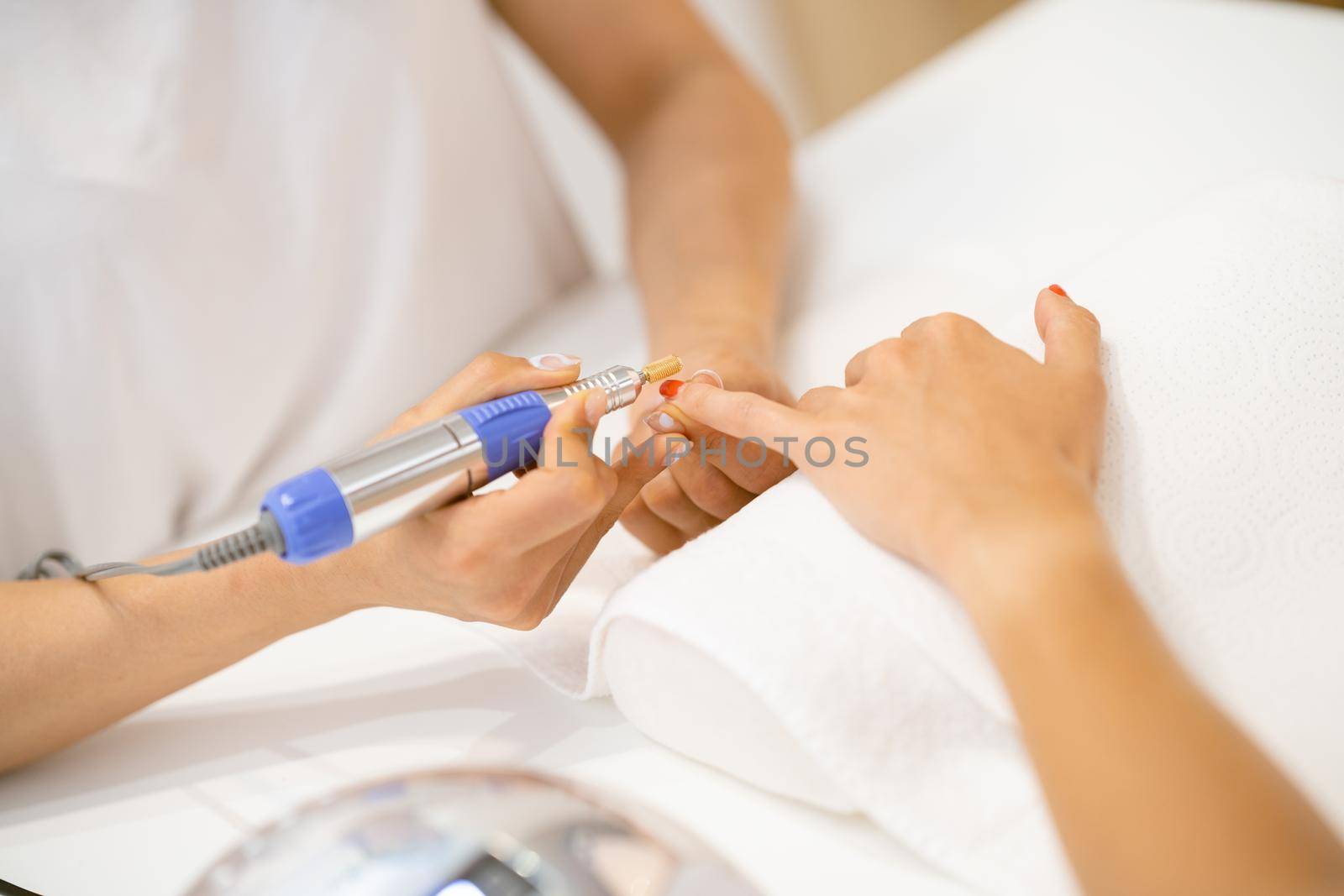 Woman in a nail salon receiving a manicure by a beautician with. Beautician file nails to a customer.