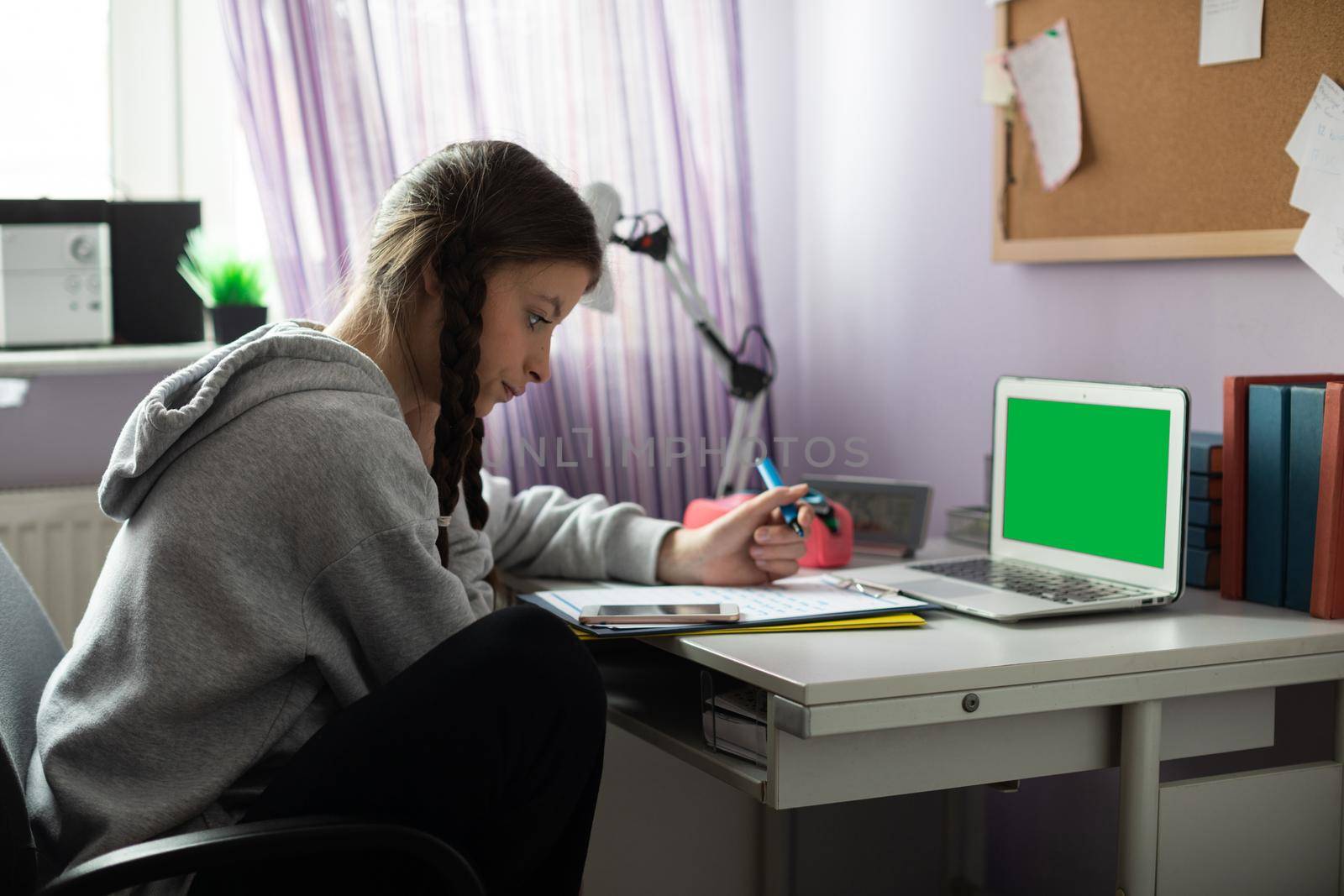 Green screen on laptop. At home in her room, a teenager sits at her desk solving assignments from school. A diligent student. Remote learning at home.