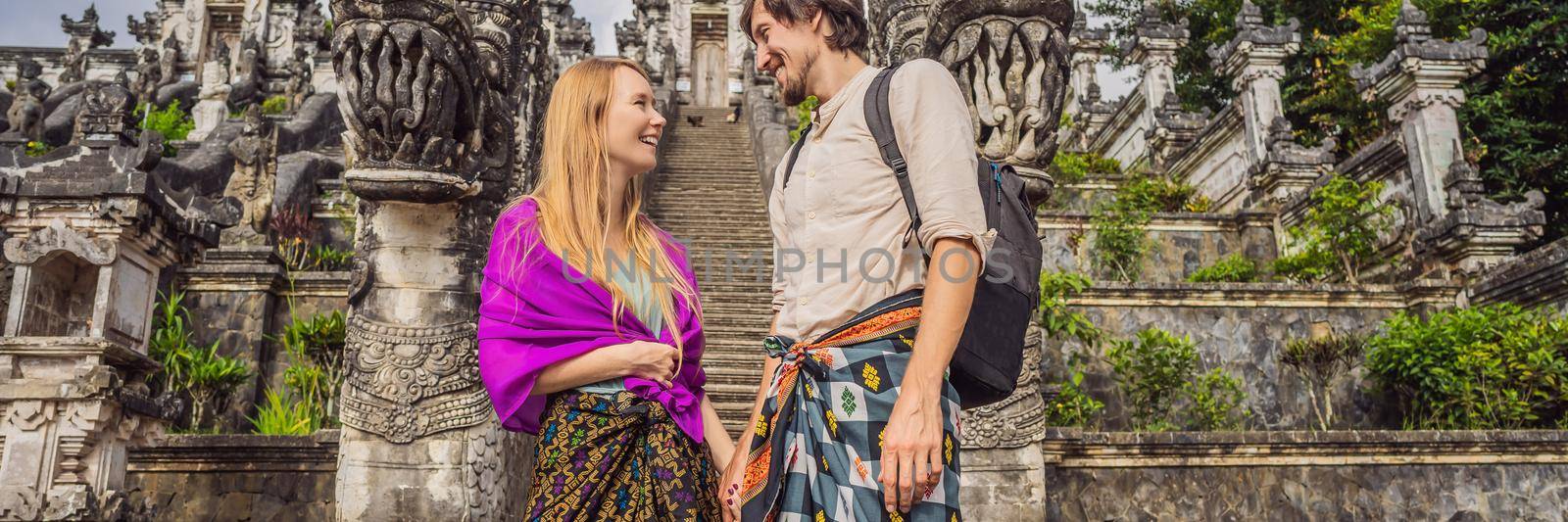 BANNER, LONG FORMAT Happy couple of tourists on background of Three stone ladders in beautiful Pura Lempuyang Luhur temple. Summer landscape with stairs to temple. Paduraksa portals marking entrance to middle sanctum jaba tengah of Pura Penataran Agung, Bali.