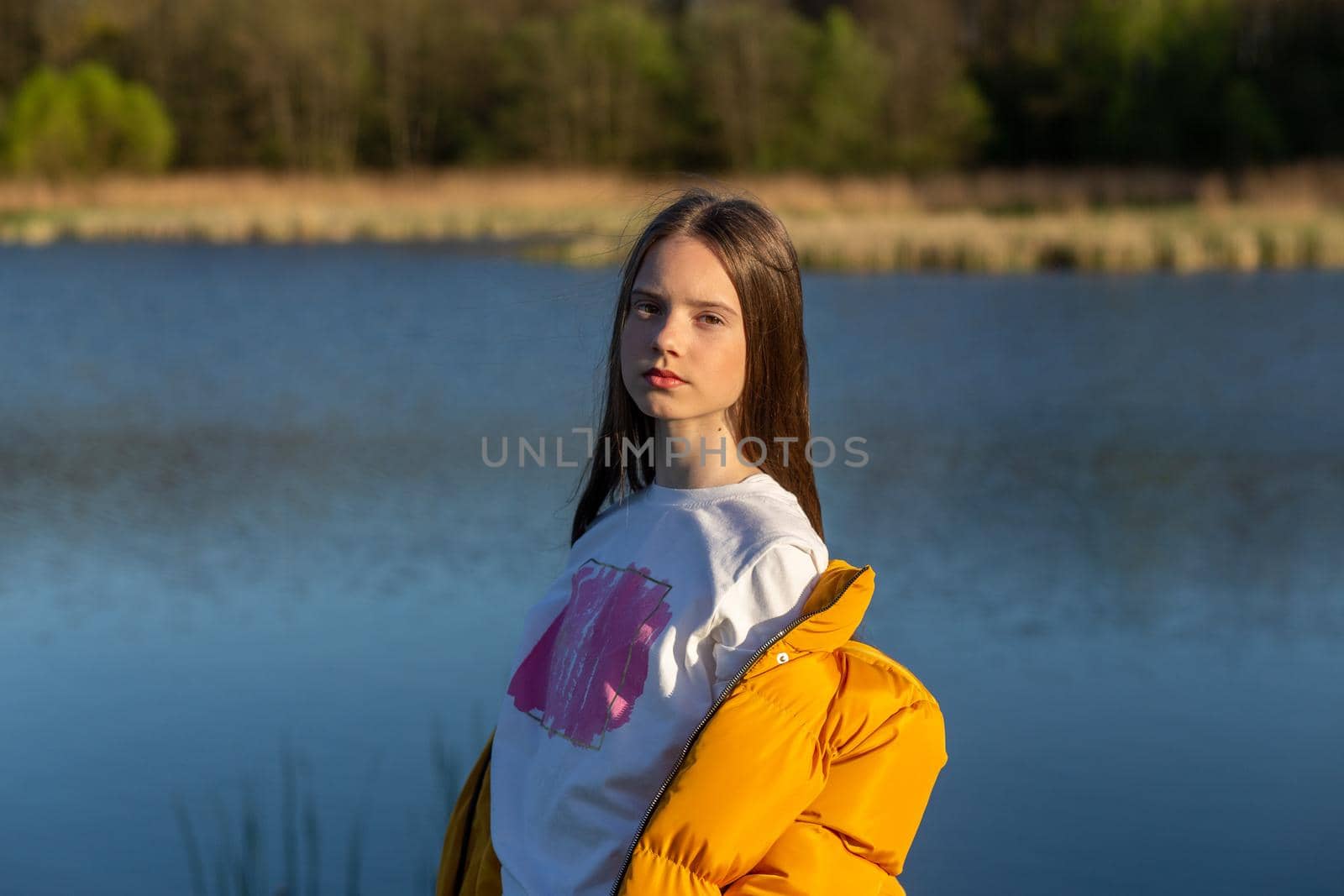 Portrait of stylish weared teenage girl outdoors in spring. A girl poses on lakes shore.