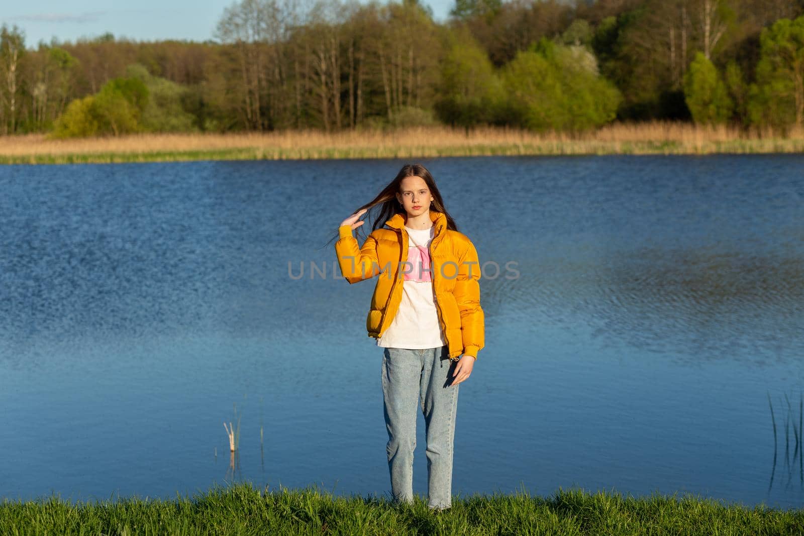 Portrait of stylish weared teenage girl outdoors in spring. A girl poses on lakes shore.