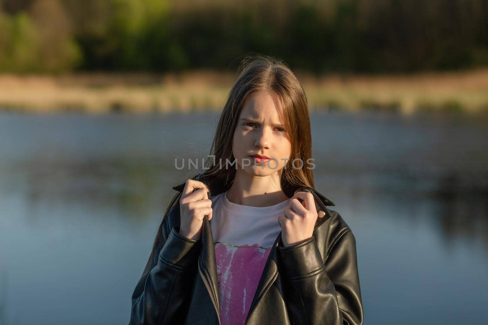 Portrait of a beautiful happy teenage girl outdoors in spring. A girl poses on lakes shore.