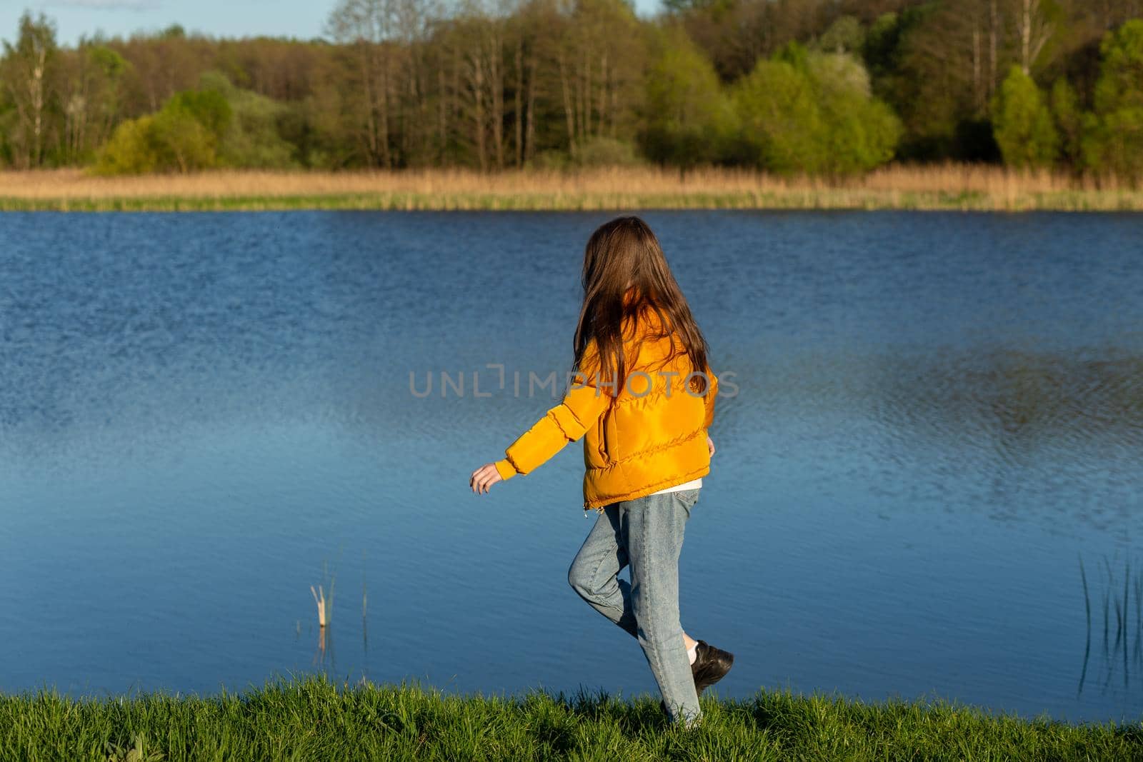 Portrait of stylish weared teenage girl outdoors in spring. A girl poses on lakes shore.