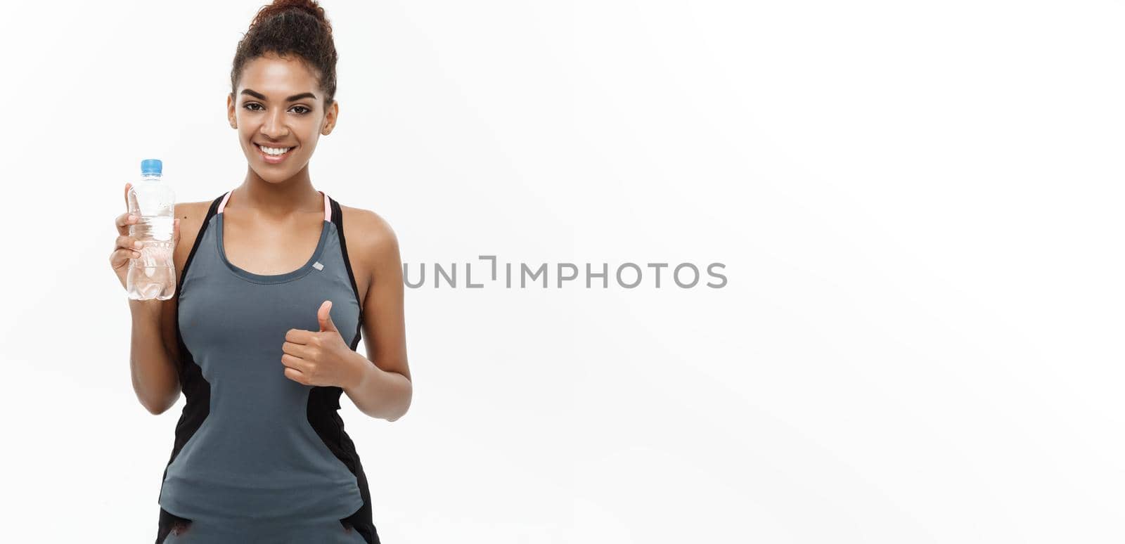 Healthy and Fitness concept - beautiful African American girl in sport clothes holding plastic water bottle after workout. Isolated on white studio background.