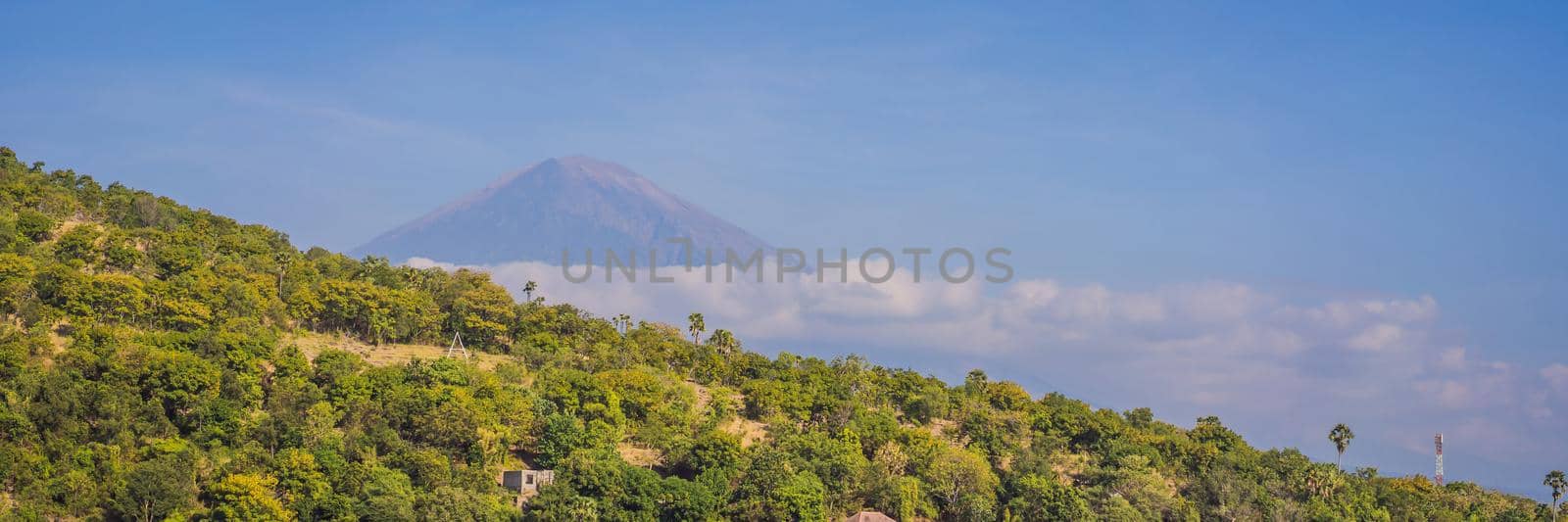 Aerial view of Amed beach in Bali, Indonesia. Traditional fishing boats called jukung on the black sand beach and Mount Agung volcano in the background, partially covered by clouds. BANNER, LONG FORMAT