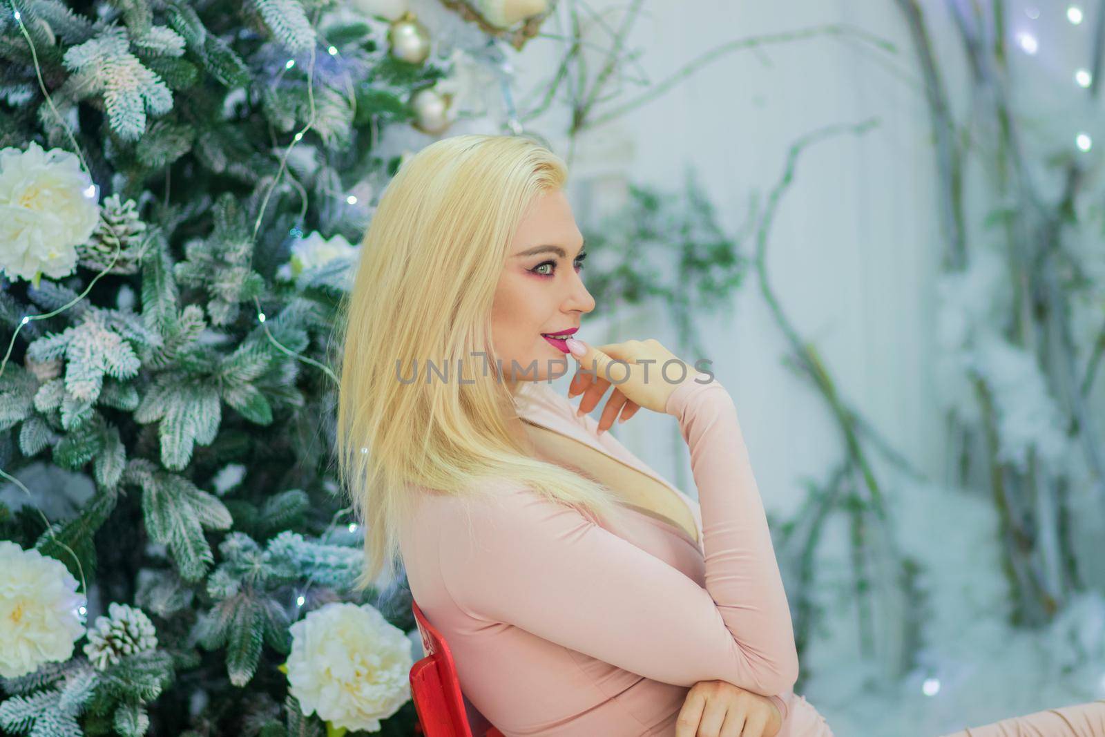 Blonde woman sit on red chair over christmas tree by Bonda