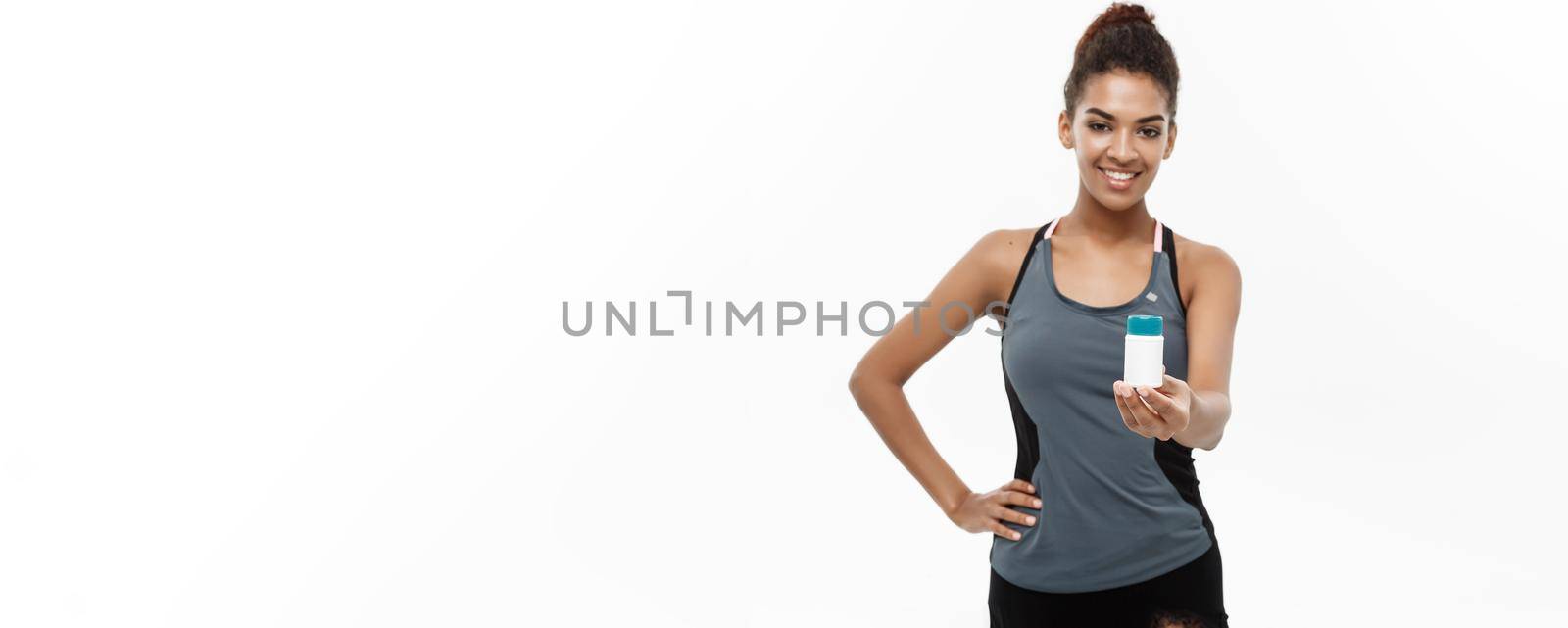 Healthy and healthcare concept - portrait of beautiful sporty African American holding bottle of supplementary bottle. Isolated on white studio background. by Benzoix