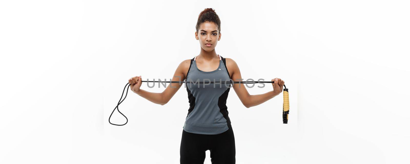 Sport, training, lifestyle and Fitness concept - portrait of beautiful happy African American woman exercising with jumping rope. Isolated on white studio background