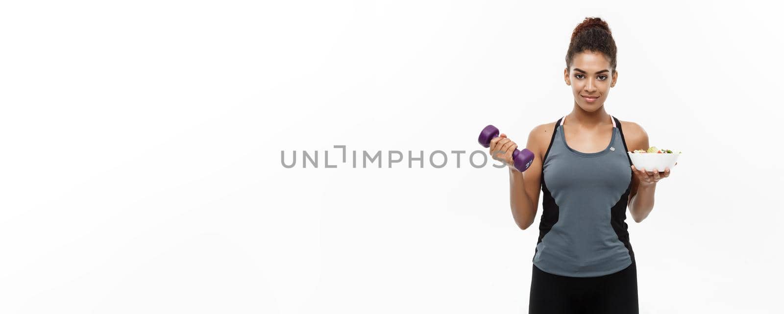 Healthy and Fitness concept - Beautiful sporty African American on diet holding dumbbell and fresh salad on hands. Isolated on white studio background. by Benzoix