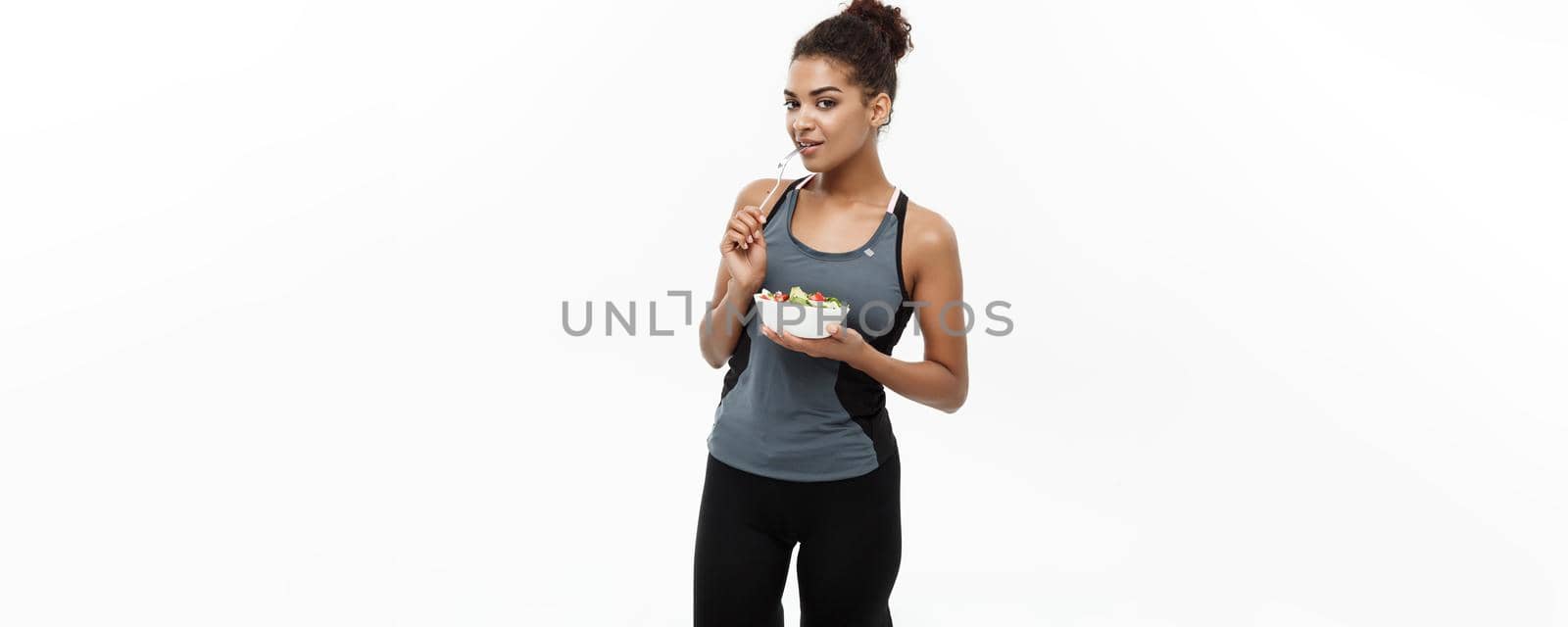 Healthy and Fitness concept - Beautiful American African lady in fitness clothes on diet eating fresh salad. Isolated on white background. by Benzoix