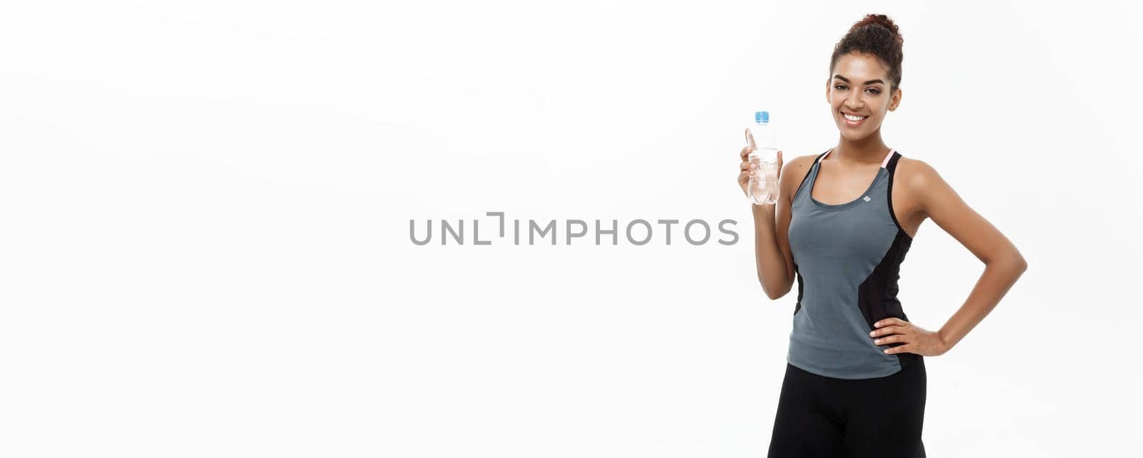 Healthy and Fitness concept - beautiful African American girl in sport clothes holding plastic water bottle after workout. Isolated on white studio background by Benzoix