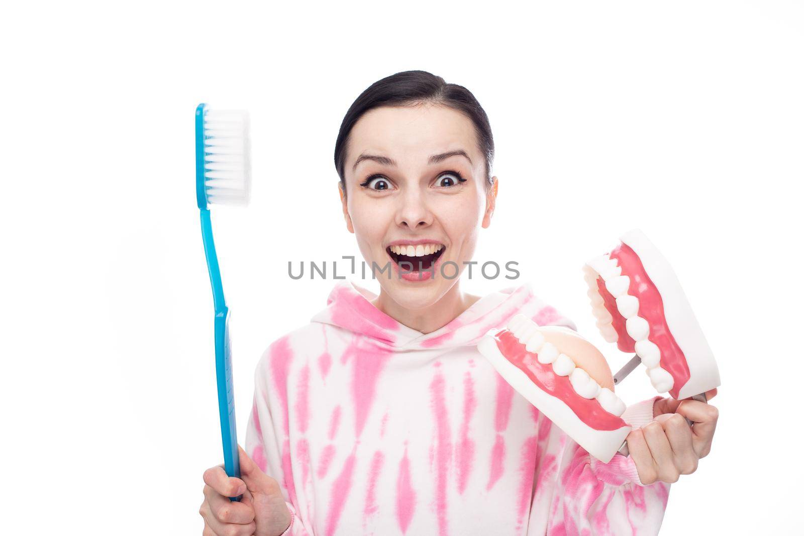 a woman in a pink sweatshirt with a huge blue toothbrush and a tooth jaw in her hands. High quality photo