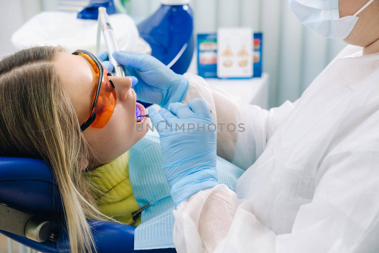 A young beautiful girl in dental glasses treats her teeth at the dentist with ultraviolet light. filling of teeth by Lobachad