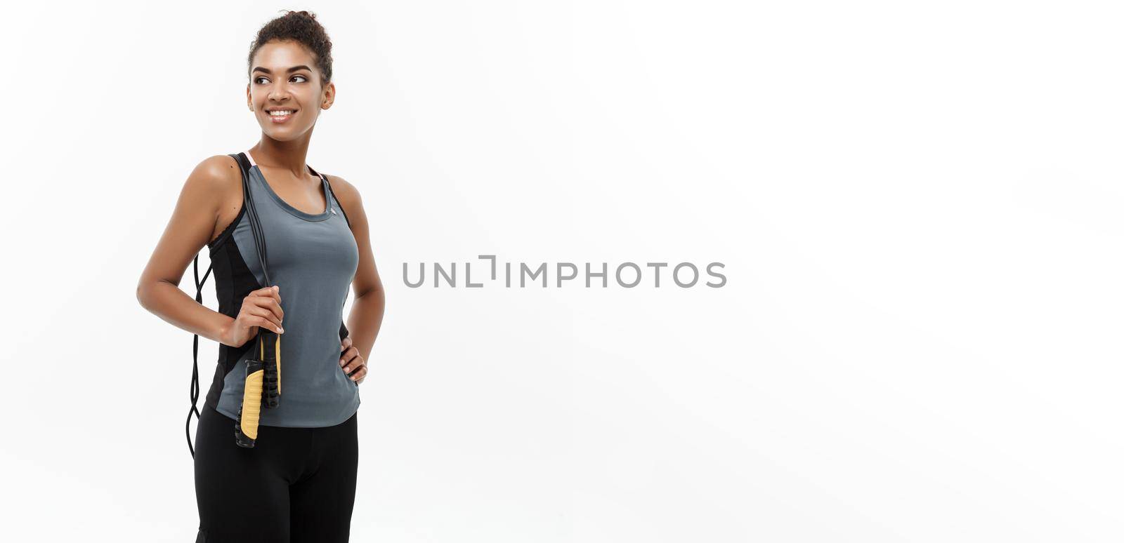 Sport, training, lifestyle and Fitness concept - portrait of beautiful happy African American woman exercising with jumping rope. Isolated on white studio background