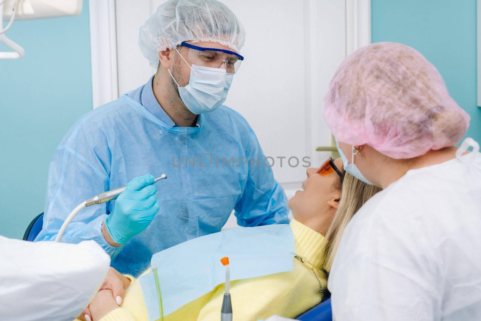 The patient smiles in the dentist's chair in a protective mask and instrument before treatment in the dental office.