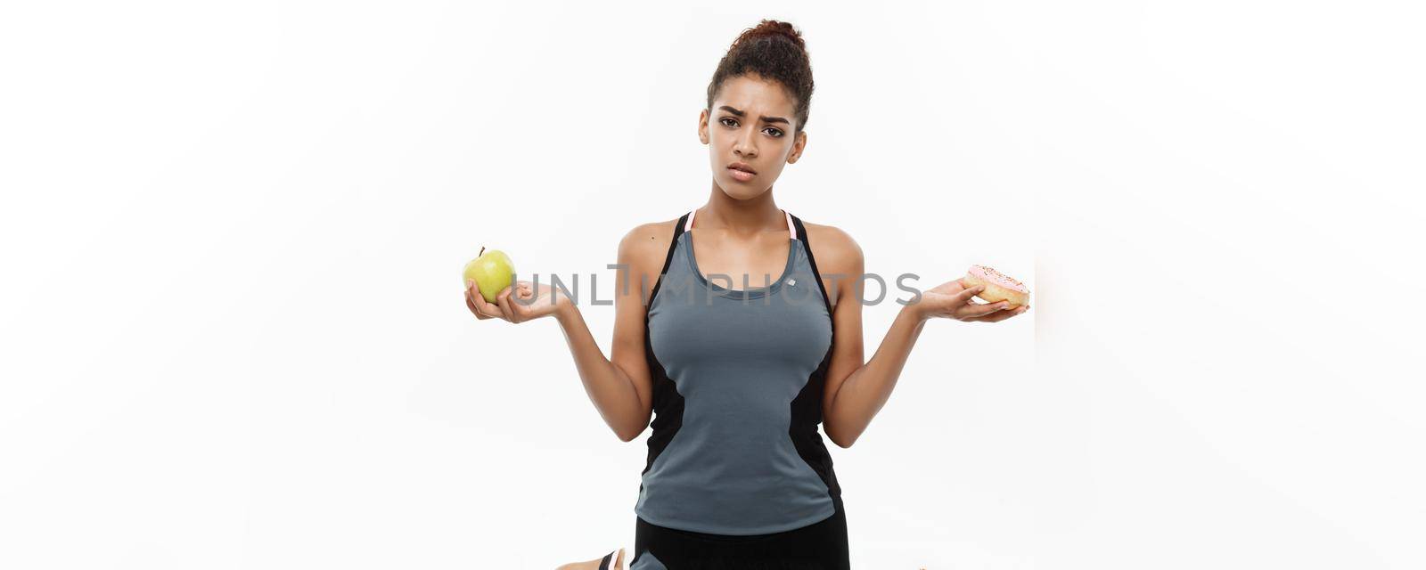 Healthy and diet concept - Beautiful sporty African American make a decision between donut and green apple. Isolated on white background. by Benzoix