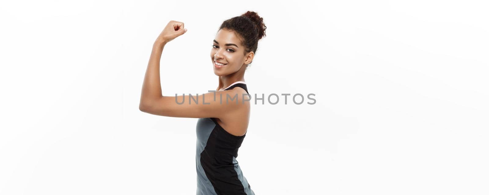 Healthy and Fitness concept - Portrait of young beautiful African American showing her strong muscle with confident cheerful facial expression. Isolated on white studio background. by Benzoix