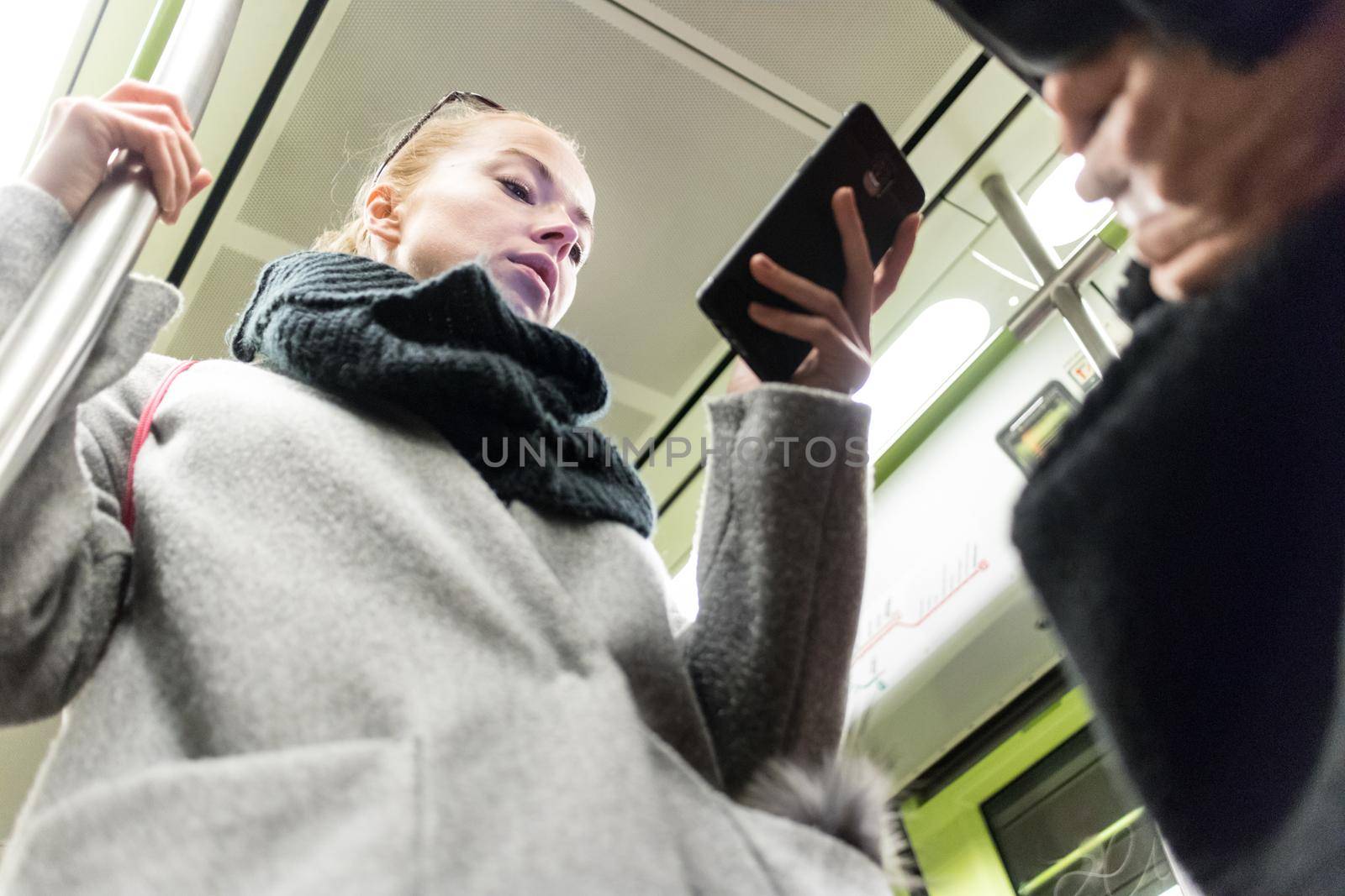 Young woman passenger using smartphone while moving in the modern metro, commuting by public transport.