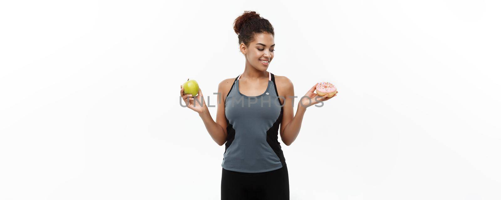 Healthy and diet concept - Beautiful sporty African American make a decision between donut and green apple. Isolated on white background