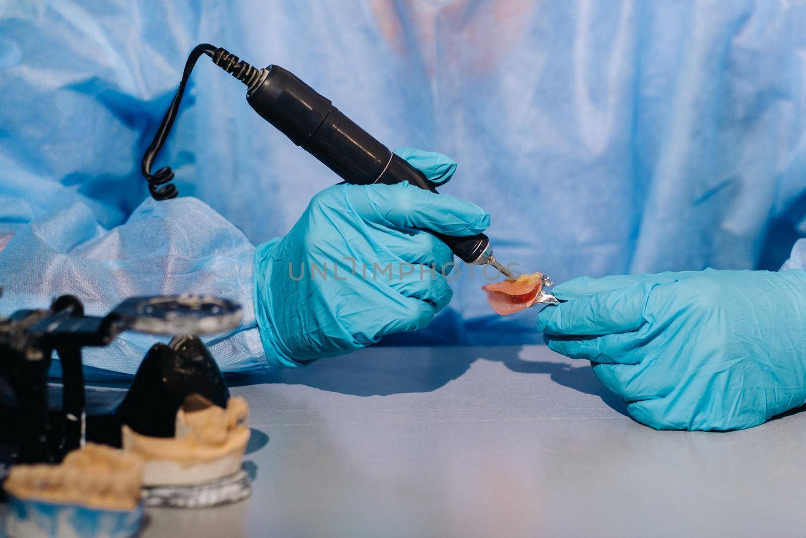 A masked and gloved dental technician works on a prosthetic tooth in his lab by Lobachad