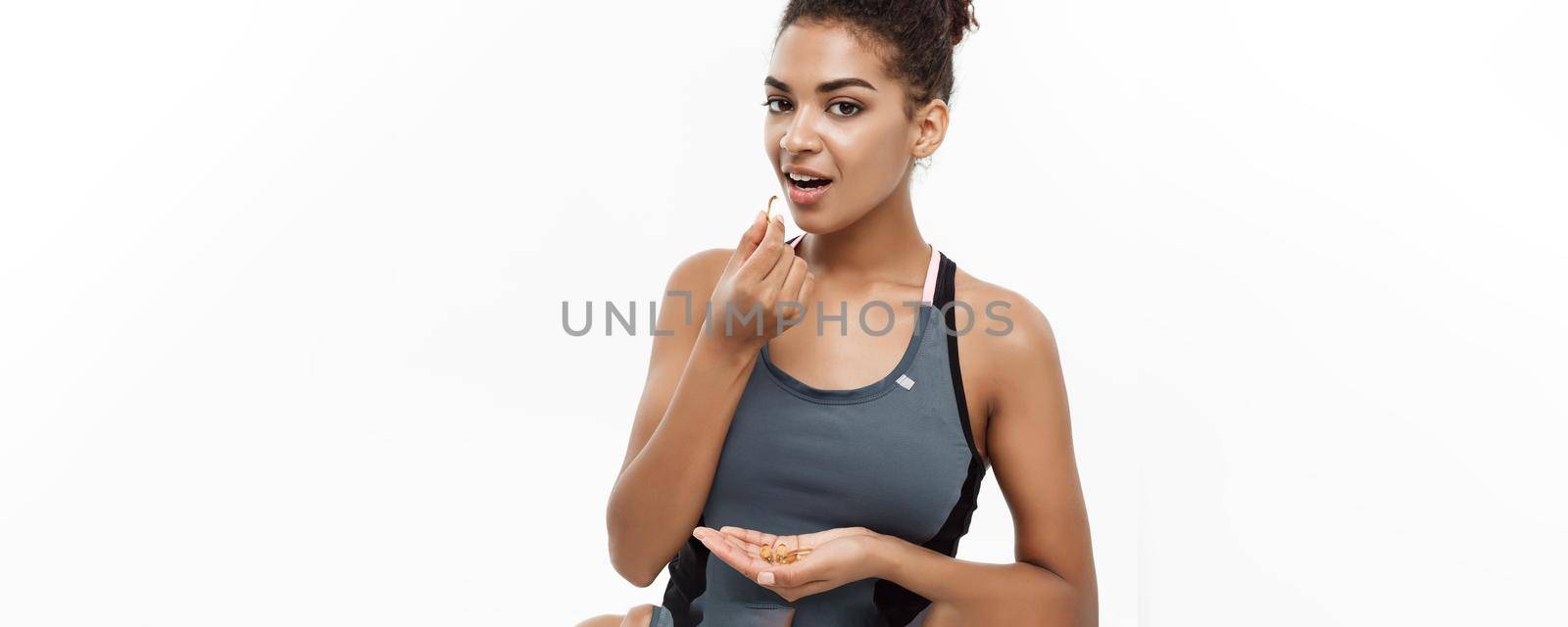 Healthy and Fitness concept - Closeup portrait of beautiful African American taking a pill of Cod liver oil. Isolated on white studio background. by Benzoix